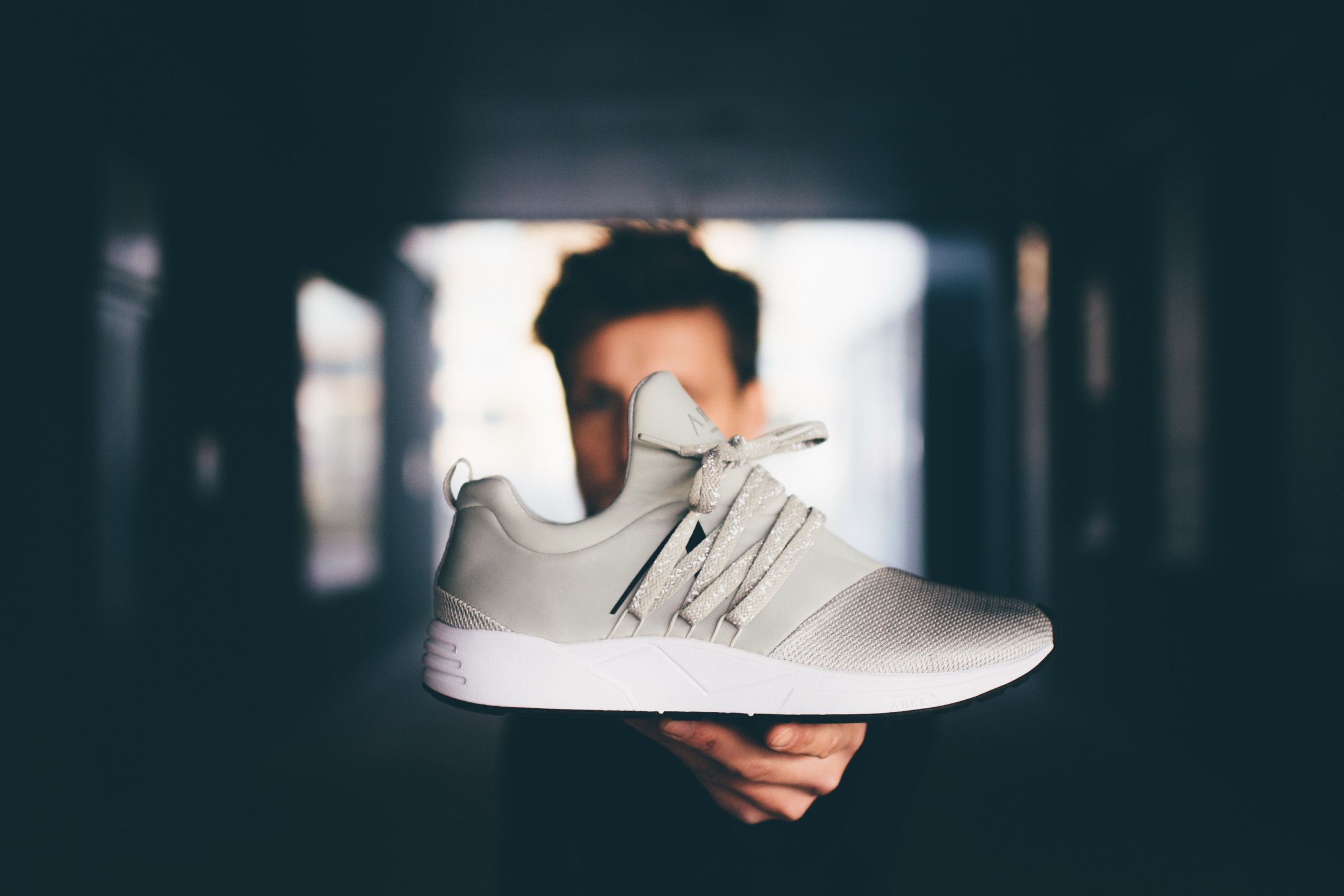 Beige ARKK sneaker held up in one hand