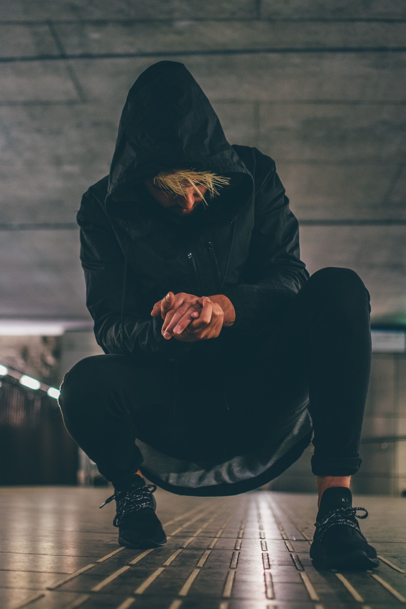 Person squatting in black, wearing ARKK sneakers