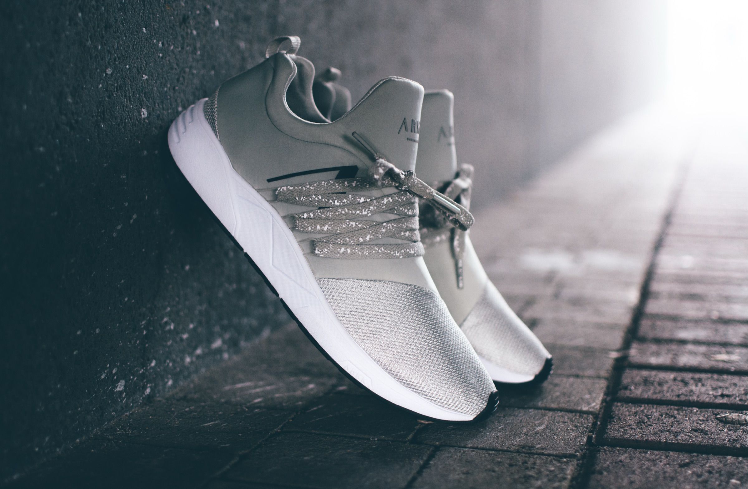 Person in ARKK sneakers leaning against a wall